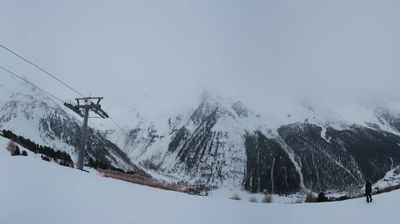 Alpine ski resort — ski lift tower against snow-covered peaks disappearing into low cloud, Ortler range, South Tyrol