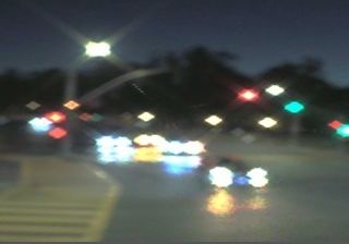 Blurry traffic camera at El Camino Real and Embarcadero — lights turned to diamond halos by camera distortion, dusk, Palo Alto