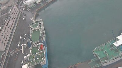 Aerial view straight down at Tomarin Harbour — water surface, pier edge, ferries, rooftops