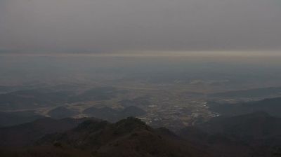 View south from mountains near DMZ — vast hazy valley, folded ridgelines receding into mist, scattered settlements barely visible