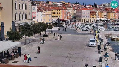 Rovinj harbor promenade, people walking along the Adriatic waterfront, boats moored, colorful old town rising behind