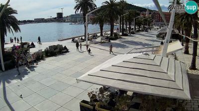 Split Riva waterfront promenade with palm trees, scattered walkers, harbor and mountains beyond