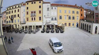 Rovinj old town main square with cafe terraces, empty chairs and tables, a few walkers, clock tower, colorful facades