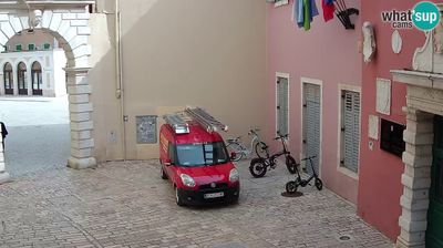 Rovinj Balbi Gate entrance to old town, narrow stone alley, red delivery van, bicycles, pink and white buildings, intimate scale