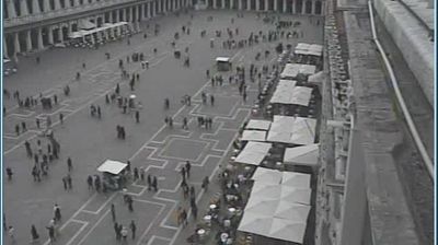 Venice Piazza San Marco from above, crowds dispersed across the piazza, cafe tent structures, the arcade of the Procuratie