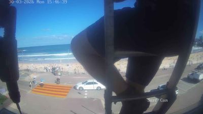 Bondi Beach surf cam — afternoon, people scattered across sand, waves, partially obscured by camera mounting pole