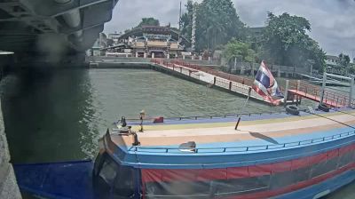 Bangkok Chao Phraya river — longboat at pier under Krung Thon Bridge, Thai flag, temple roof visible