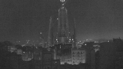 Sagrada Familia at night — dark spire rising against sky, a few lights like a constellation, cranes visible